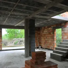 Budowa domu w stanie surowym. Widać betonowy strop, ściany z pustaków ceramicznych, schody i materiały budowlane.