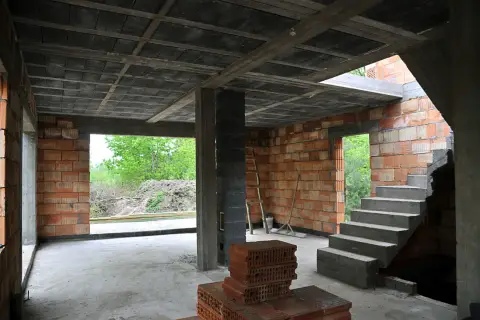 Budowa domu w stanie surowym. Widać betonowy strop, ściany z pustaków ceramicznych, schody i materiały budowlane.