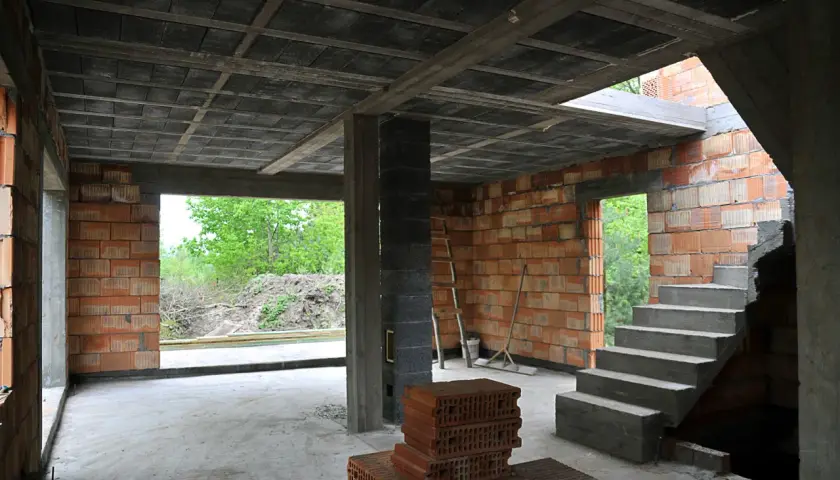 Budowa domu w stanie surowym. Widać betonowy strop, ściany z pustaków ceramicznych, schody i materiały budowlane.