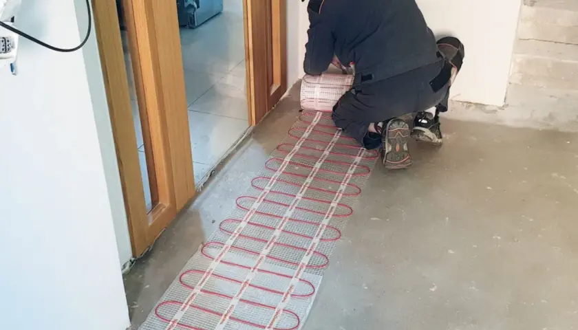 Instalator układa matę grzewczą, przygotowując podłogę do montażu. To inwestycja w komfort i przyszły koszt ogrzewania podłogowego.