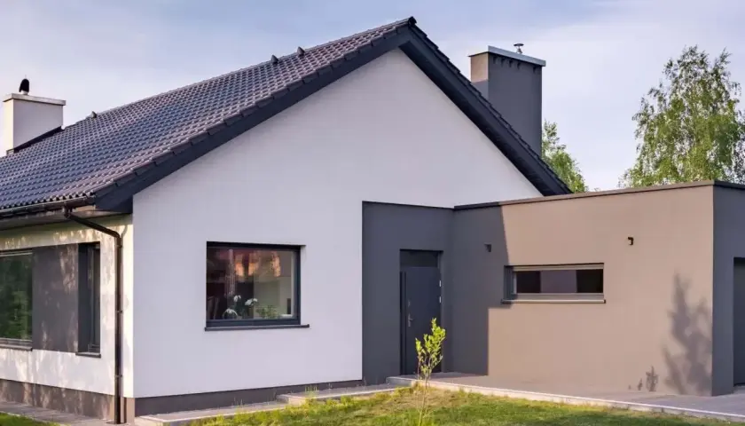 Nowoczesny dom z białym tynkiem i szarym dachem. Elegancki cokół na elewacji podkreśla jego architekturę.