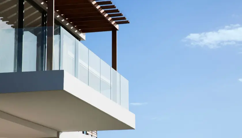 Nowoczesny balkon z przeszkloną balustradą i drewnianą pergolą to świetny pomysł, czym osłonić balkon, zapewniając prywatność i cień.